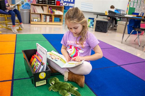 girl reading to stuffed animal on colorful carpet